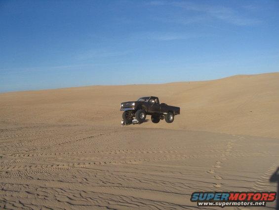 Dark 1985 Ford Ranger jumping over a sand dune