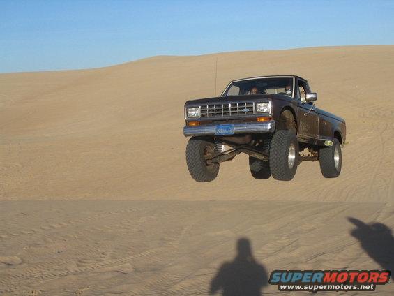 Brown 1985 Ford Ranger mid-air over a sand dune, front wheels off the ground