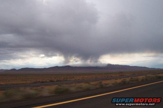 Storm clouds gathering over a mountain range with a highway in the foreground