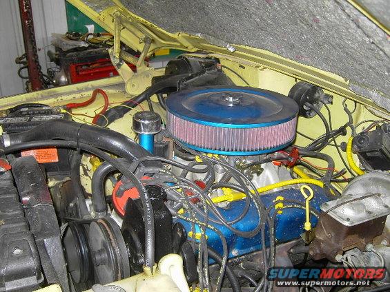 Yellow engine bay with blue air filter, distributor, and valve covers. Wires and hoses are visible