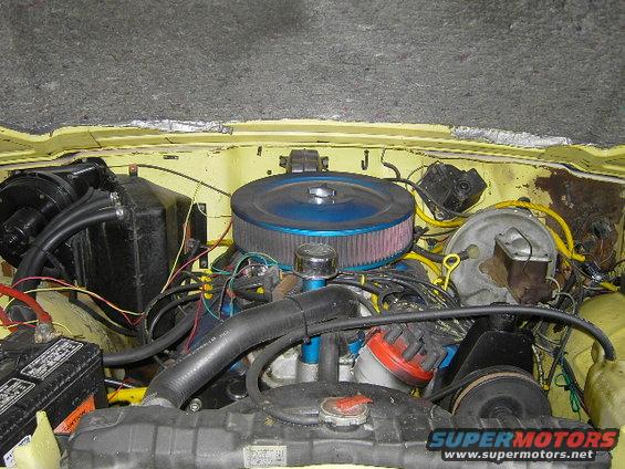 Engine bay with blue air filter, yellow wiring, and black components. Hood insulation is visible at the top