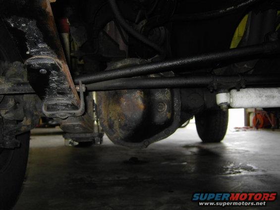 Undercarriage view of a vehicle's front axle and differential, with visible rust and suspension components