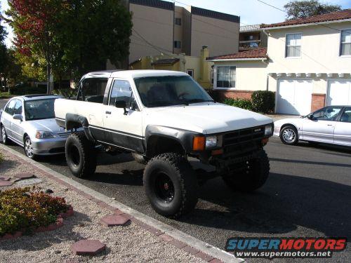 Lifted white 1985 Toyota 4Runner parked on street, silver sedan to its left, white coupe to its right