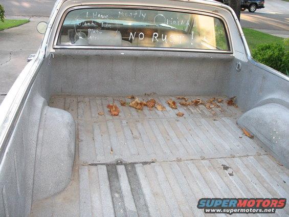 1966 Ford Ranchero bed, light-colored, with writing on the rear window and scattered leaves
