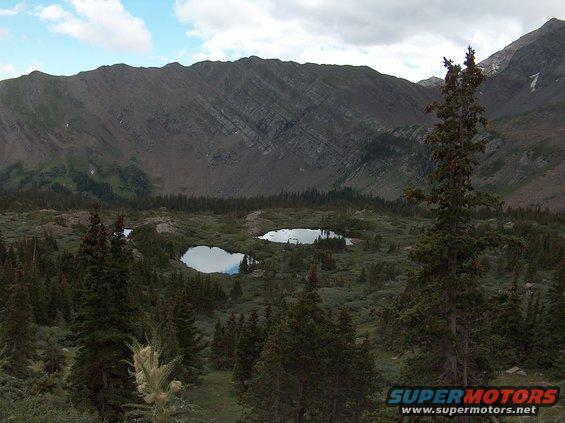 Mountain range overlooks two small lakes surrounded by pine trees and scrub brush
