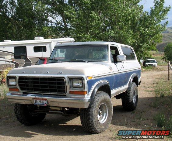 Ford Bronco with blue stripe, parked next to an RV. Another white vehicle is visible in the background
