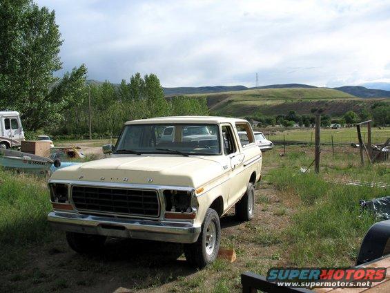 Cream-colored 1978 Ford Bronco parked in a grassy field with hills in the background