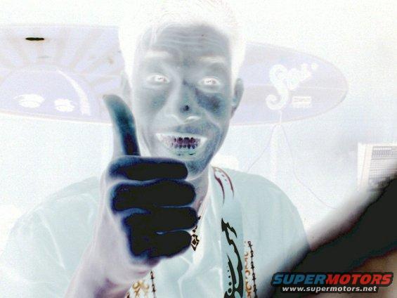Man with a thumbs up gesture, wearing a white shirt with decorative trim. Inverted colors