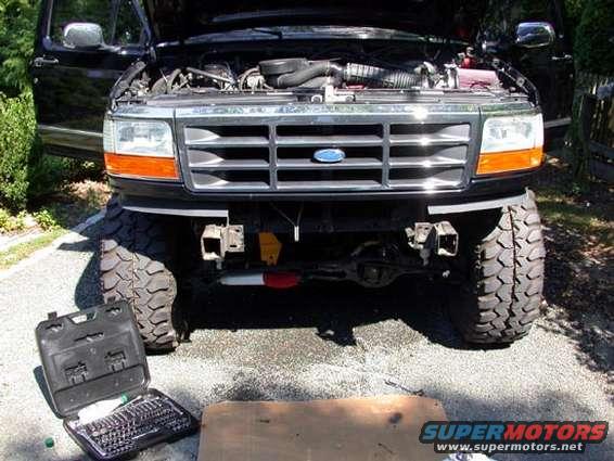 Front view of a lifted black 1995 Ford Bronco with hood open and toolbox nearby