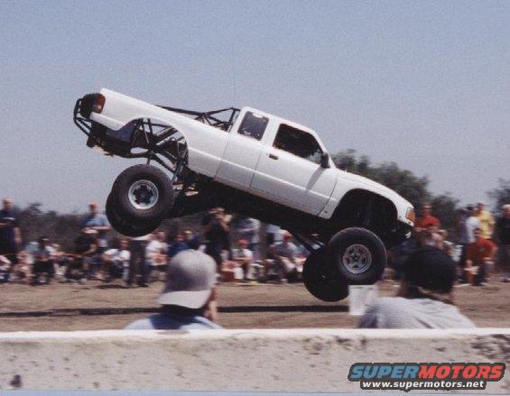 White pickup truck airborne with large tires and roll cage