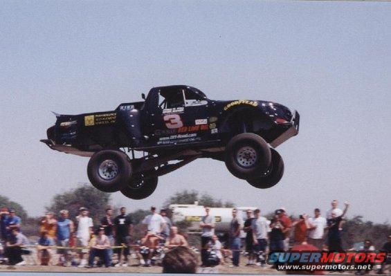 Black off-road race truck with number 3 and Goodyear tires airborne over a crowd