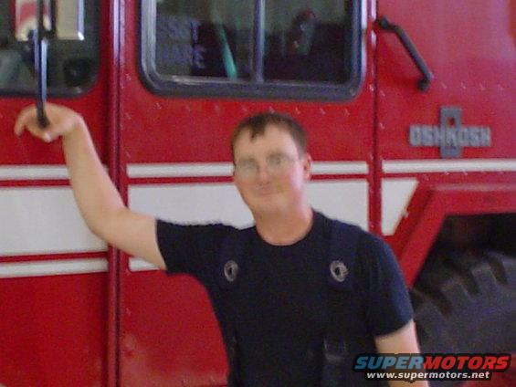 Red fire truck with white stripes and a man leaning on it