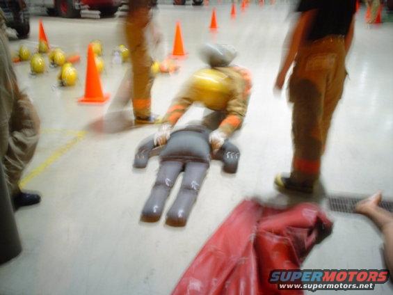 Firefighters practice with a dummy on the floor, surrounded by cones and helmets