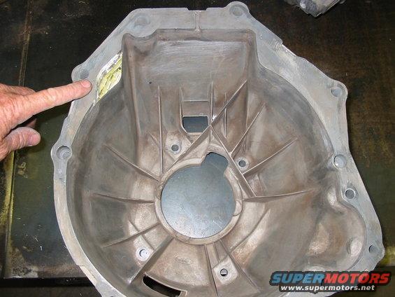 Close-up of a metal transmission bell housing with a finger pointing to a damaged area
