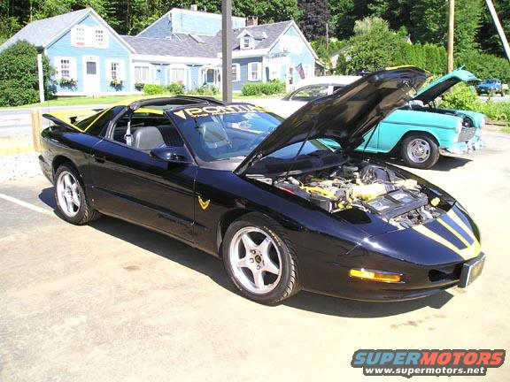 Black 1994 Pontiac Firebird Trans Am with yellow stripes, hood open, parked next to a teal 1950s car
