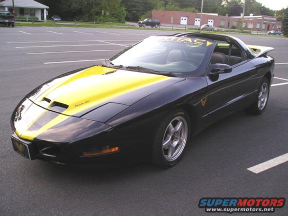 Black and yellow 1994 Pontiac Trans Am with racing stripes on hood and roof, parked in a lot