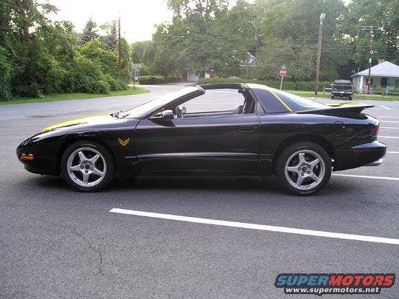 Black convertible sports car with a yellow stripe on the hood and rear spoiler, parked on asphalt