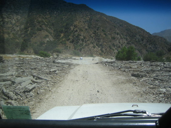 White SUV driving on a dirt road with debris, mountains in background