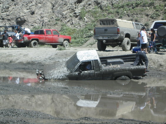 Truck stuck deep in mud, with other vehicles and people nearby