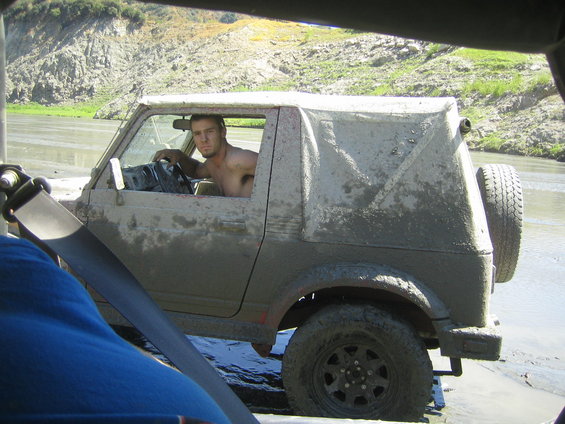 Driver in a mud-covered 1987 Suzuki Samurai stuck in water