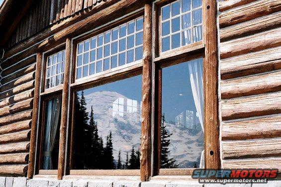 Log cabin exterior with large windows reflecting a snow-capped mountain and evergreen trees