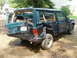 1978 Ford F-250 - This heavily damaged dark green Jeep Cherokee shows significant rear-end impact, with the tailgate and rear quarter panel severely deformed.