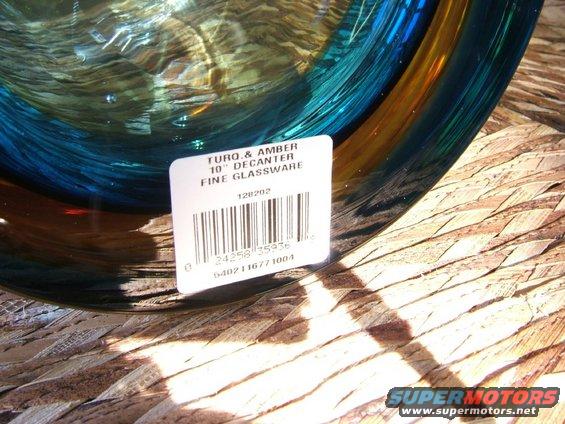 Glass decanter with blue and amber tones, on a woven surface, with a product label