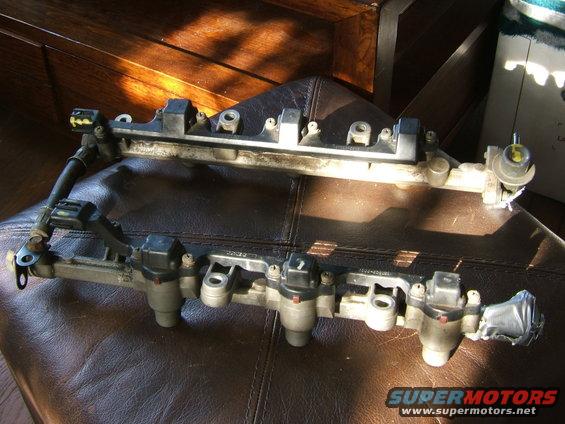 Fuel rail with injectors on a brown surface. Supermotors.net logo visible