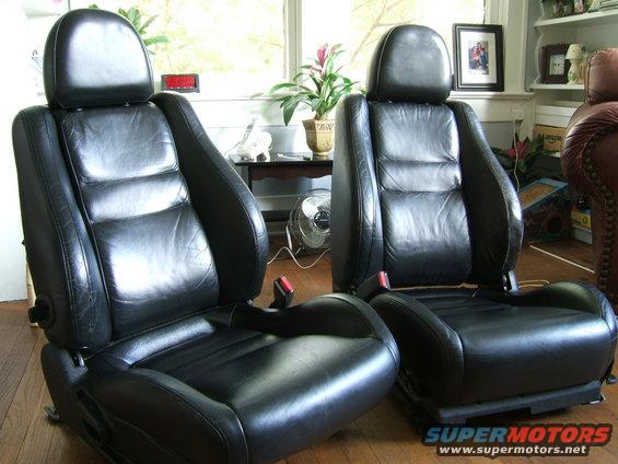 Two black leather car seats with headrests and seatbelts
