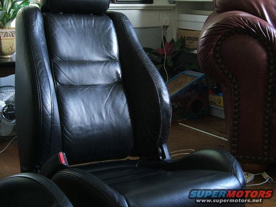Black leather car seats with red seatbelt buckle visible. Another leather chair is in the background