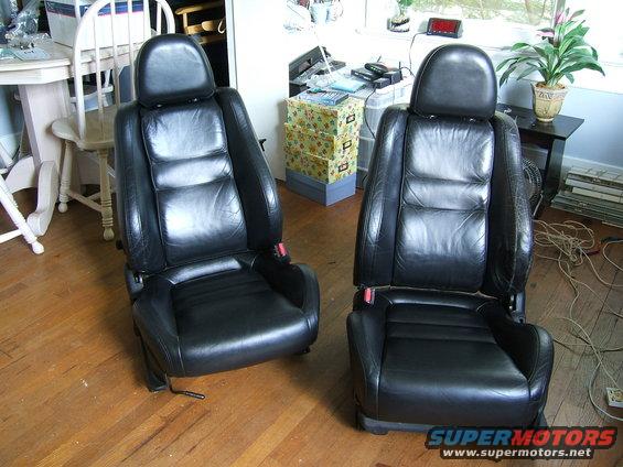 Two black leather car seats with headrests and red seatbelt buckles