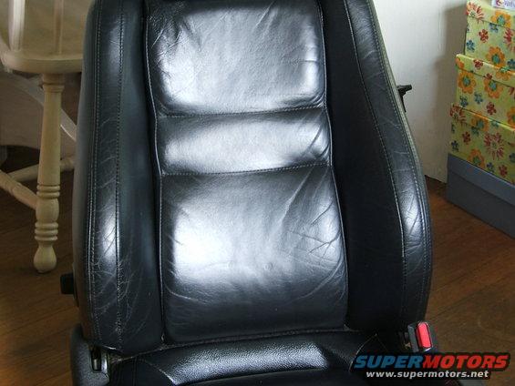 Black leather car seat with visible wear and stitching, red seatbelt buckle visible