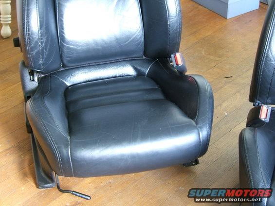 Black leather car seats with visible wear and tear, showing seat adjustment levers and seatbelt buckles
