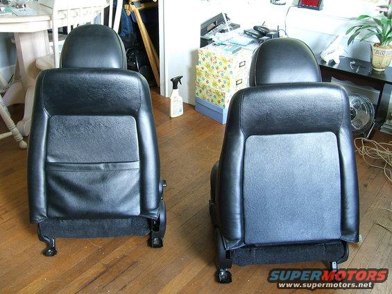 Two black leather car seats with headrests are on a wooden floor. A spray bottle is to the left of the right seat