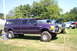 2006 Ford Supercrewzer - A lifted purple 2006 Ford F-250 Super Duty pickup truck with a camper shell is displayed at an outdoor event.