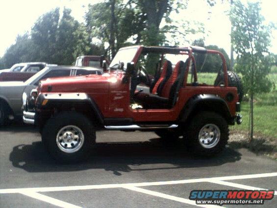 Red Jeep Wrangler with black interior, side view, parked on asphalt