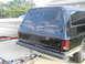 1990 Chevrolet Suburban - Rear view of a black SUV, possibly from the 1980s, hitched to a trailer. A white boat on a trailer is parked nearby.