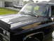 1990 Chevrolet Suburban - A black 1990 Chevrolet Suburban shows significant paint degradation on its hood, with another white SUV visible in the driveway.
