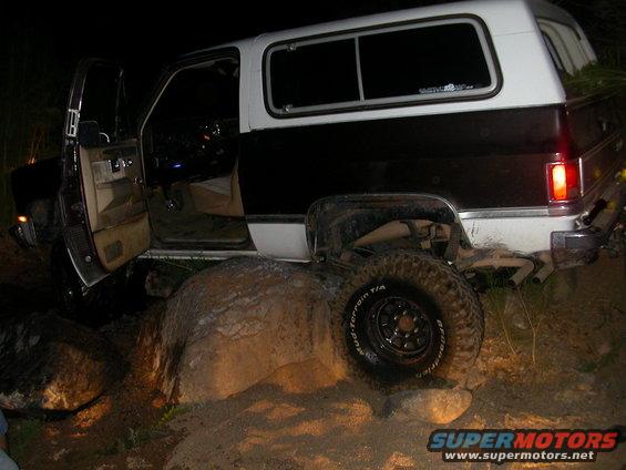 Off-road vehicle with open driver door on rocks at night. The vehicle has a two-tone black and white body