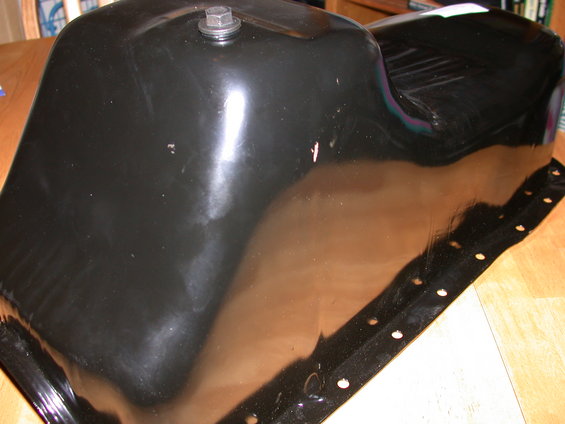 Black metal oil pan with bolt on top, resting on a wooden surface