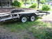 1997 Ford Crown Victoria - A dual-axle car hauler trailer sits on grassy ground near a building.