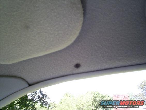 Close-up of a car's headliner with a sun visor visible. A small dark spot is on the headliner
