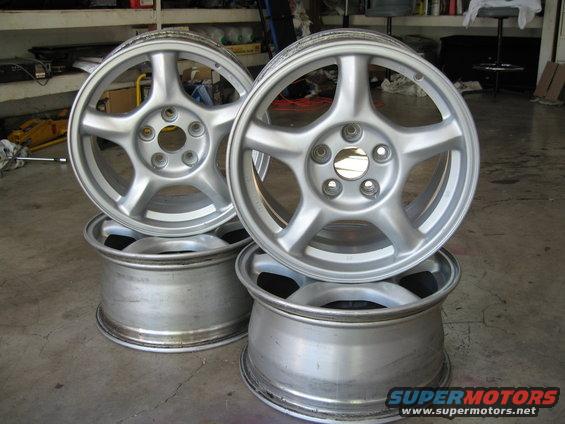 Four silver 5-spoke alloy wheels stacked in a garage