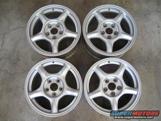 Four silver alloy wheels with five spokes each, arranged on a concrete floor