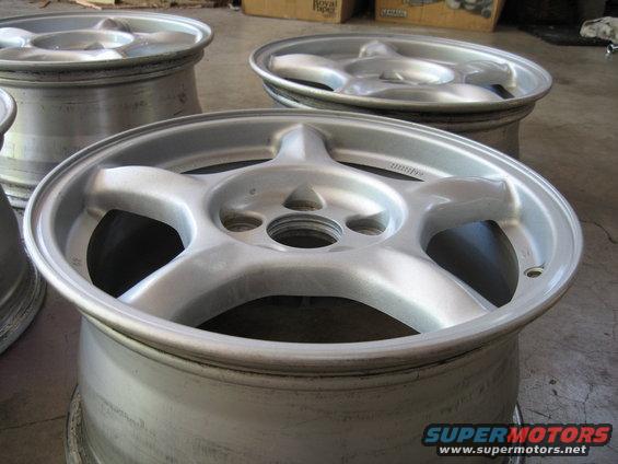 several silver 5-spoke car wheels stacked up