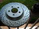 1969 Ford Mustang - A close-up view of a slotted and drilled brake rotor and caliper, likely an aftermarket upgrade for improved performance.