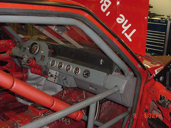 Race car interior with gray dashboard, gauges, and red roll cage