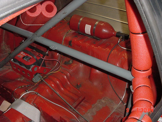 Interior of a red car with a roll cage, nitrous oxide tank, and battery