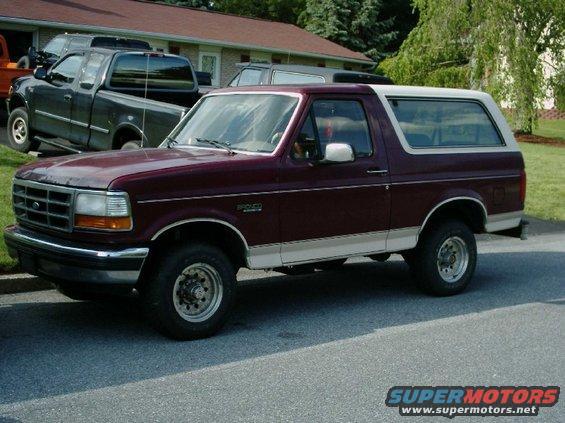 Maroon Ford Bronco parked on street, dark pickup truck behind it