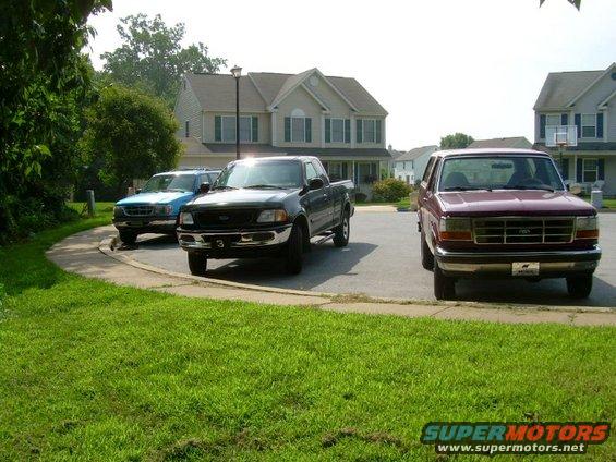 Maroon 1997 Ford F-250 parked in front of a house, with a black Ford F-150 and a blue Ford Ranger behind it